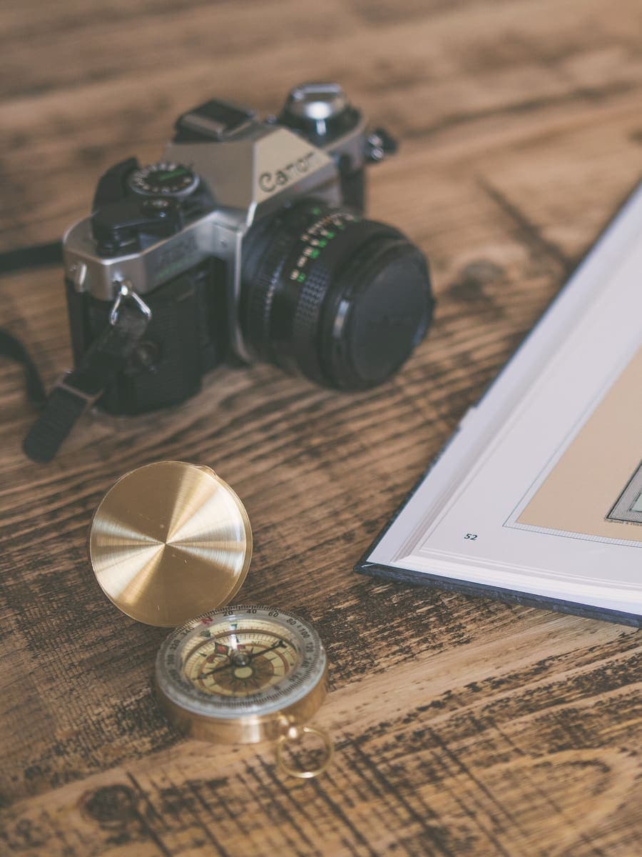 A camera, compass and atlas laid out on a wooden table